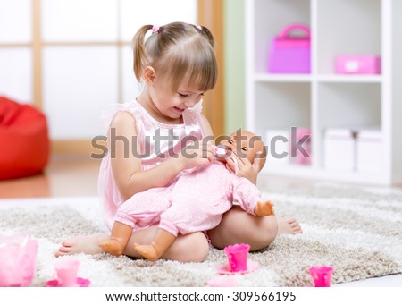 Cheerful little girl playing with doll in preschool