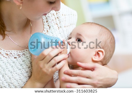 Young mother at home feeding their baby with milk bottle, feeling proud