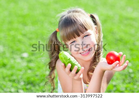 Happy child girl sitting on the grass with vegetables at day time. Concept of healthy food.