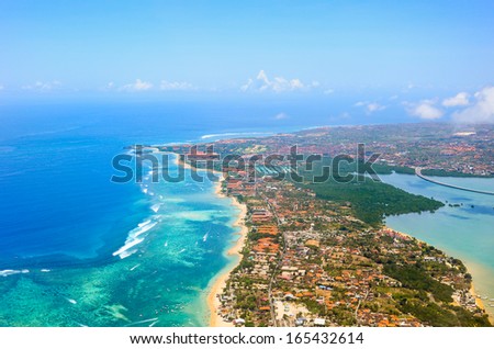Sandy coast, buildings and blue sea with waves. Bali island view from plane