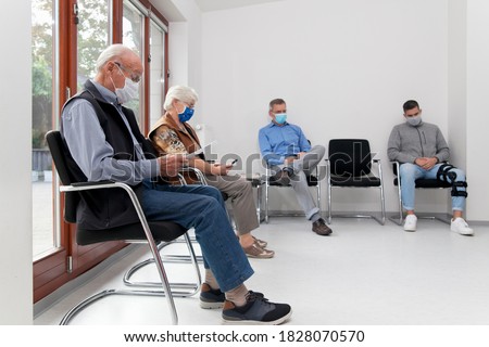 Senior couple with face masks sitting in a waiting room of a hospital together with a young and mature man - focus on the old man in the foreground Foto stock © 