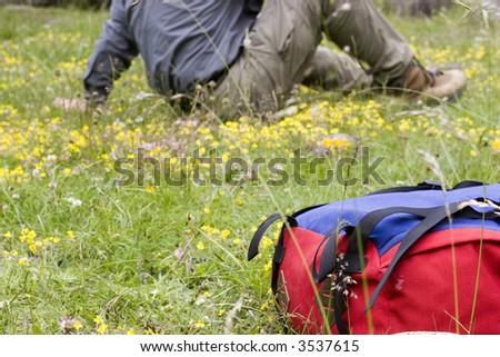 Mountaineer having a rest in a meadow in the mountains - focus on the rucksack in the foreground