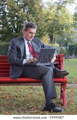 Businessman working with a laptop while sitting on a red bench in a park