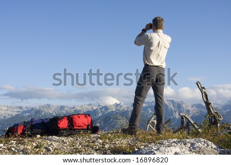 Mountaineer looking through field glasses while standing on a mountain peak