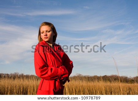 A young attractive girl stands alone in a corn field wearing a red bright coat
