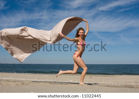 A girl runs along a beach flying a silk sheet