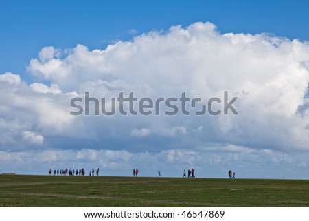 People walking along the horizon with a large cloud overhead