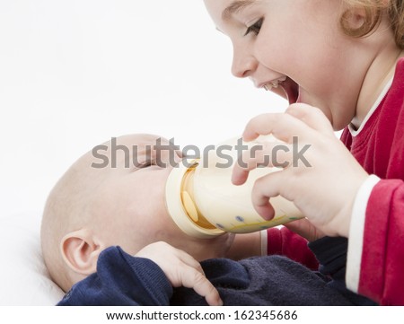 young, happy child feeding toddler with milk bottle in light background