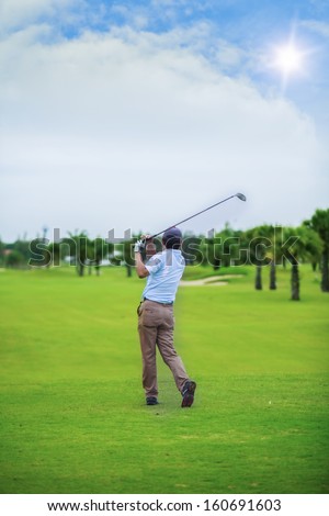 Male golf player teeing off golf ball from tee box, wonderful cloud formation in background.