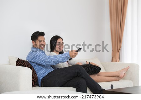 Young Asian couple watching television at home in living room