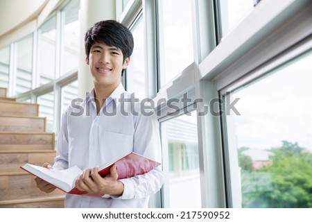 Happy Asian male student holding books at the library