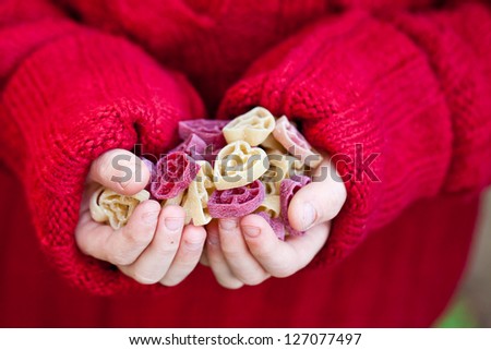 Kid, holding heart shaped red and white raw pasta. Also available in vertical format.