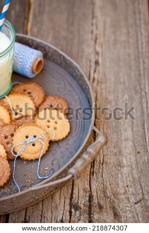Sugar cookies in shape of buttons on wooden table with a glass of milk.  Also available in horizontal format. Copy space.