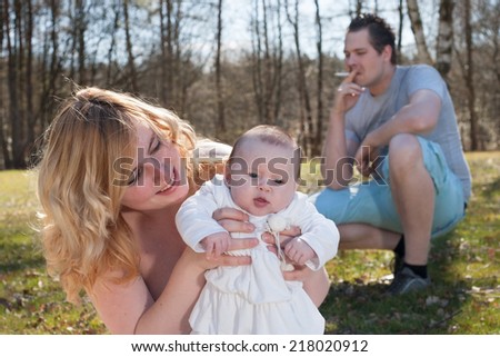Young father is smoking while its unhealthy for his family. Distance between father and family