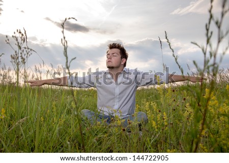 Relaxing guy, sitting in the grass on the summer meadow.