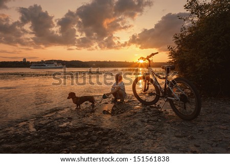 Boy with dog at the riverbank observing cruise boat