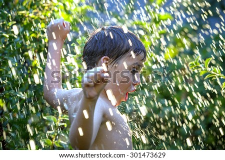 Summer fun. Excited 11-years boy in the water shower at the garden. Water drops in sunlight.