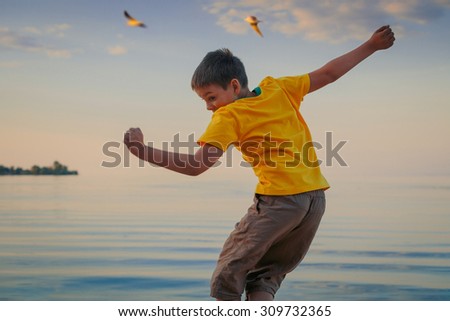 Fun boy jumping on a summer river bank.