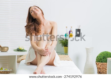 health and beauty concept - woman in spa salon seating on the massage desk