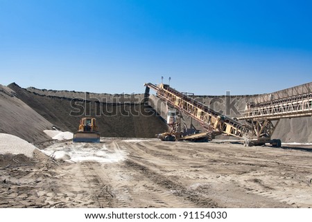 a large conveyor belt carrying golden ore and emptying onto a huge pile