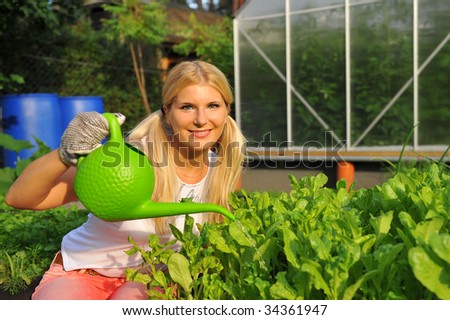 Young smiling blond girl working in the garden watering salad plant