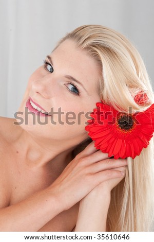 Pretty natural blond girl enjoying aroma of red gerber flower