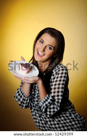 young beautiful girl eating small sweet cake. yellow background. copy-space. focus on the cake