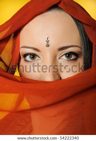 Young beautiful woman eyes in indian traditional jewellary, bindi , sari dress and makeup. yellow background