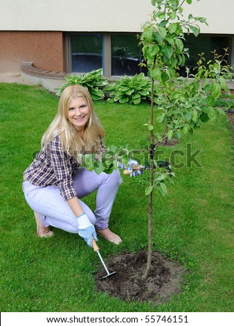 Pretty gardener woman with gardening tools outdoors planting apple tree