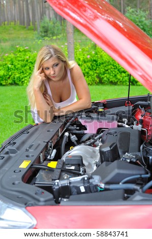 Young beautiful woman standing near red car and looking under hood confused on the engine and other car details
