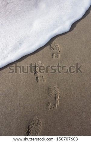 A line of boot prints in the sand are washed away by incoming surf