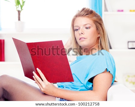Young blond woman reading book at home