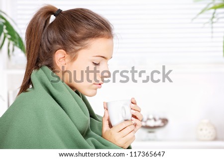 pretty young woman drinking tea  at home covered with blanket