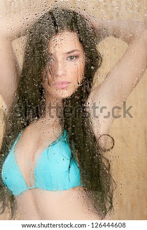 Pretty woman in bikini behind glass full of water drops