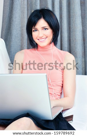 Pretty young woman with headphones and laptop on white sofa at home