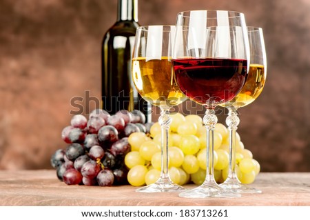 cups of red and white wine in front of grape and bottle