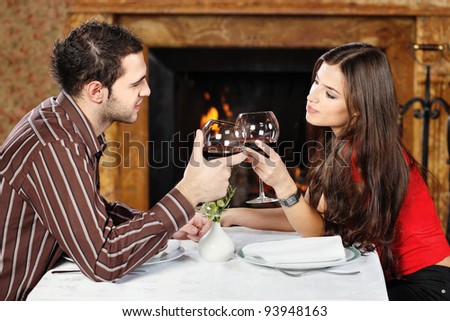 Young couple in love near fireplace, holding glasses of wine and cheers