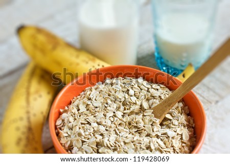 Oat flakes in orange bowl with banana and milk on wooden table. Selective focus.