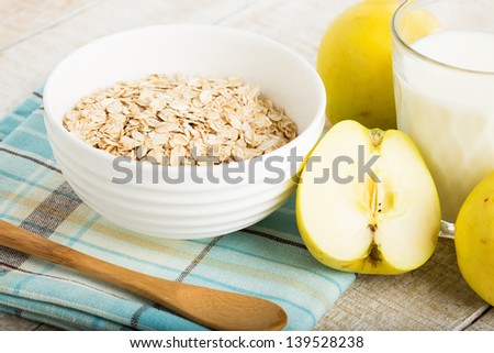 Oat flakes in orange bowl with apples  and milk on wooden table. Selective focus.