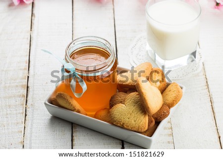 Honey, fresh milk  in glass and sweet cookies on wooden background. Selective focus.