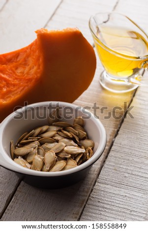 Pumpkin seeds, pumpkin, oil  in bowl on white wooden table. Selective focus.
