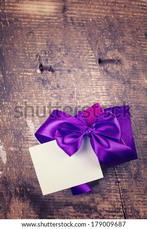 Festive gift box with bow with empty card on wooden background. Selective focus.