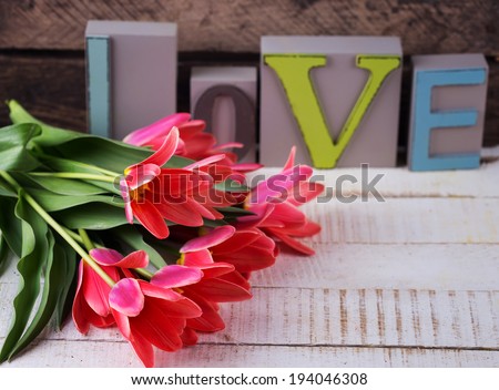 Postcard with fresh flowers tulips and word love on white wooden background. Selective focus.