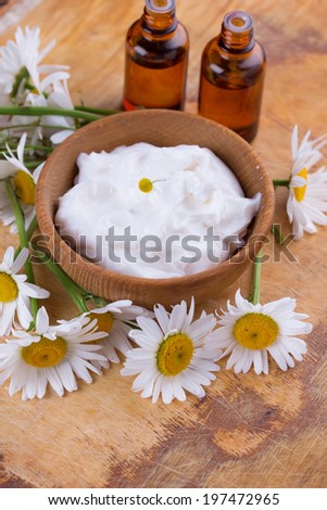 Beauty cream in bowl  with chamomile on wooden background. Selective focus, horizontal.