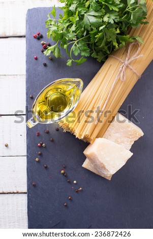 Italian food - cheese parmesan, raw pasta, olive oil  on slate  on white table. Selective focus is on piece of cheese.