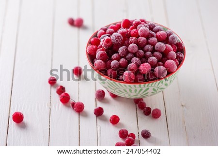 Frozen cranberry in bowl on white wooden background. Selective focus.