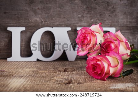 Background with fresh flowers and word love. Roses on aged wooden table. Selective focus.