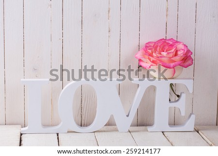 Background with fresh rose and word love.  Rose on white wooden table. Selective focus.