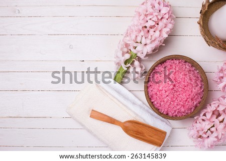 Spa  and wellness setting in pink color. Sea salt in wooden bowl, towel, flowers on white wooden background. Selective focus.Place for text.