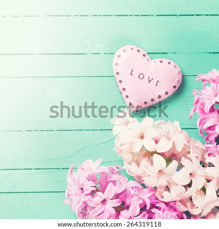 Postcard with fresh hyacinths  and  decorative heart with word love on it  on  green wooden background. Selective focus is on flowers. Place for text. Square image.